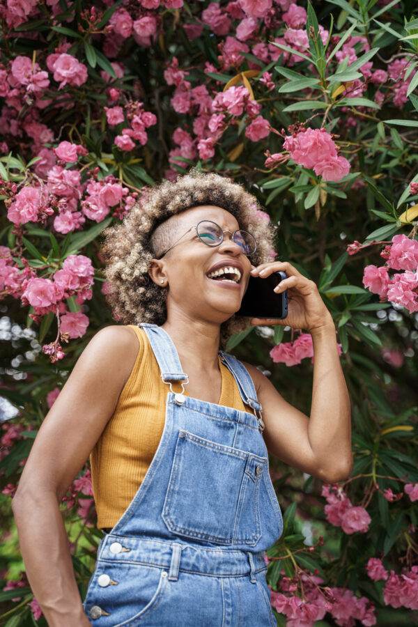 African American stylish woman smiling on a phone call surrounded by pink roses in the garden